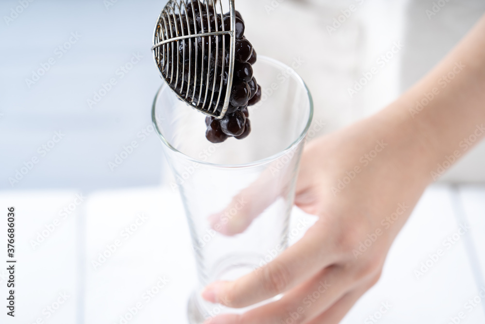 Making bubble tea, scoop and pour cooked brown sugar flavor tapioca pearl bubble balls into cup on w