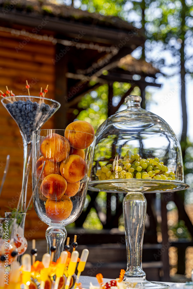 Dishes with blueberries and peaches. Fruits on party table. Grapes under glass transparent dome cove