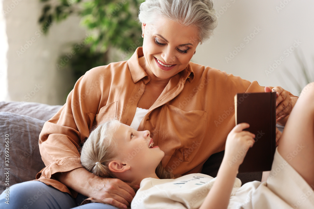 Cheerful grandmother and granddaughter reading book together.