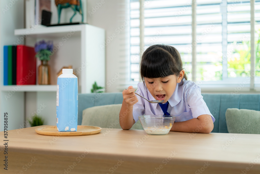 穿着制服的亚洲小学生女孩在早校吃早餐麦片配牛奶