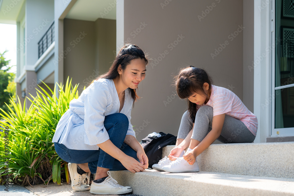 亚洲母亲帮助女儿小学生穿制服，让他们系鞋带或穿鞋