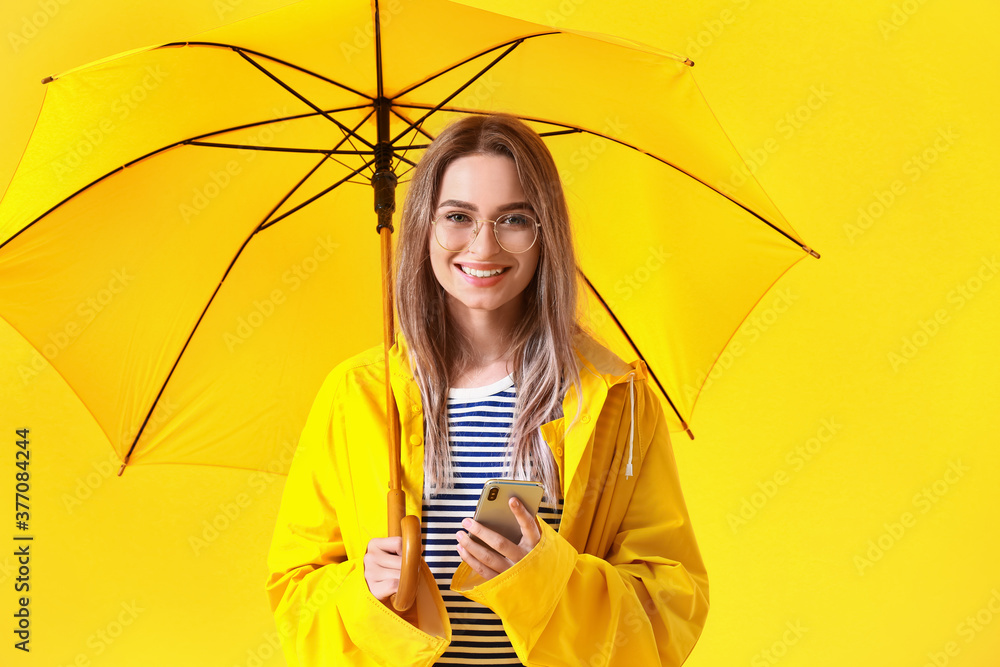 美丽的年轻女子穿着雨衣，彩色背景带伞