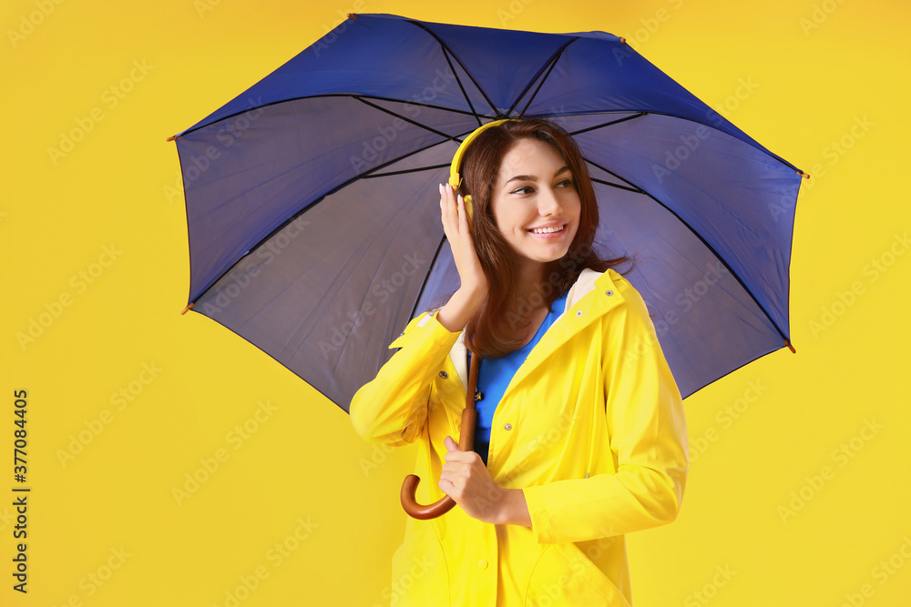 Beautiful young woman in raincoat and with umbrella on color background