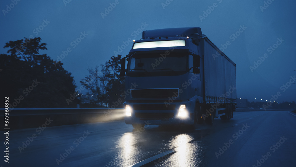 Long Haul Semi-Truck with Cargo Trailer Full of Goods Travels At Night on the Freeway Road, Driving 