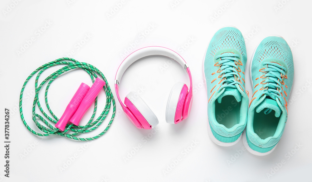 Sportive shoes, jumping rope and headphones on white background