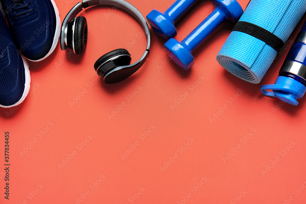 Sportive shoes, bottle of water, yoga mat, dumbbells and headphones on color background