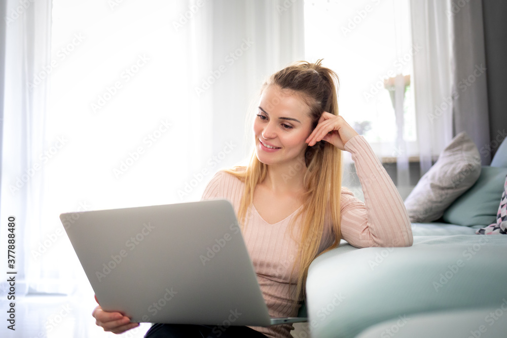 Relaxed woman enjoying time at home using laptop sitting near sofa