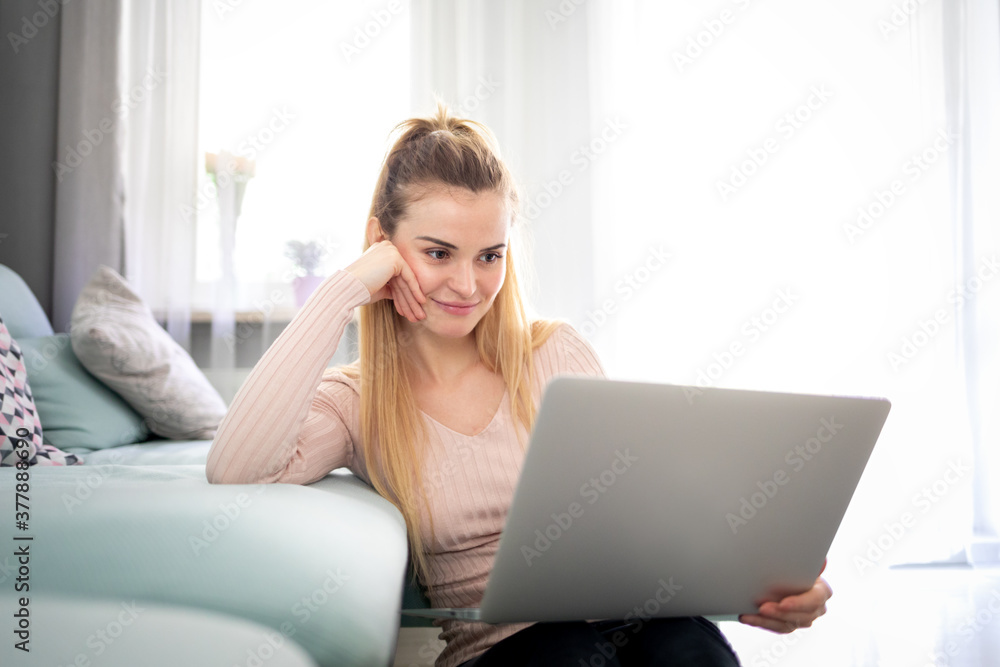 Relaxed woman enjoying time at home using laptop sitting near sofa