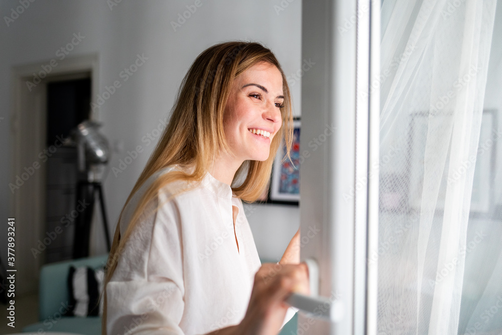 Beautiful smiling woman opening window at the morning