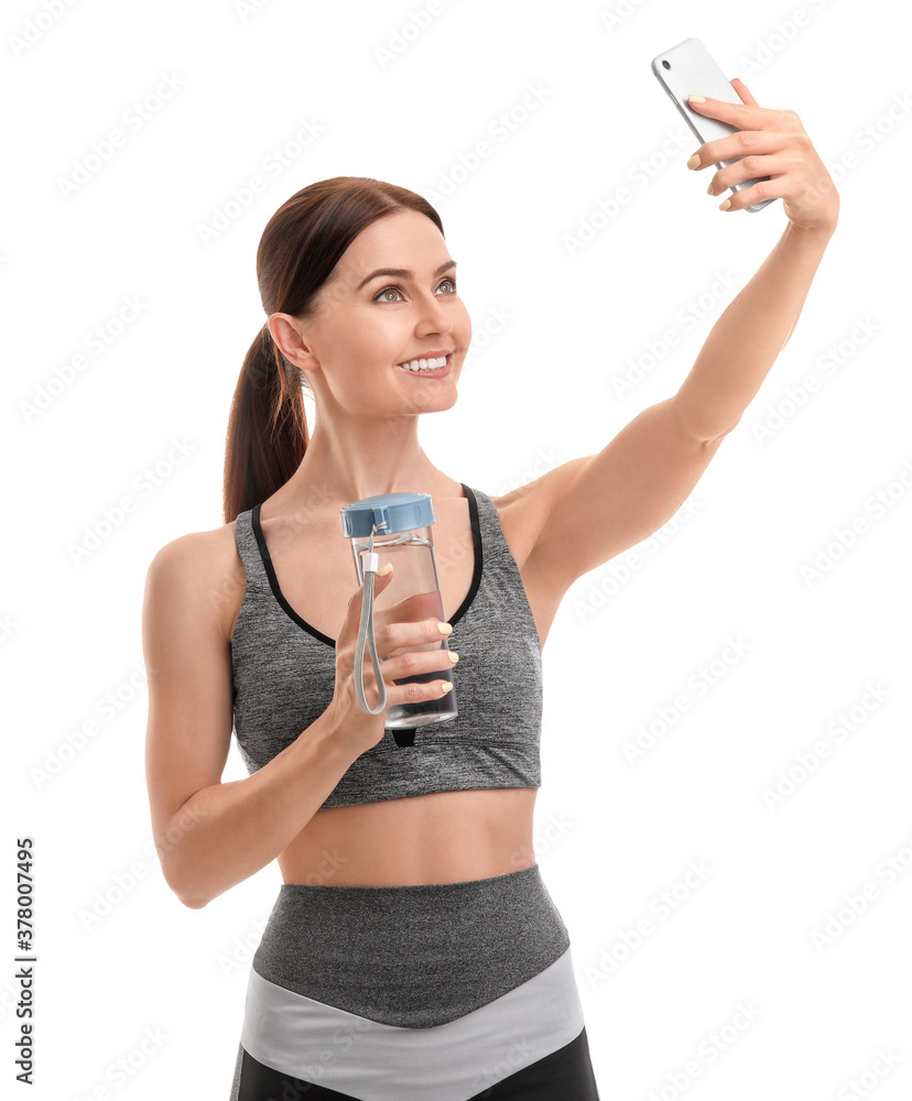 Sporty young woman with bottle of water taking selfie on white background