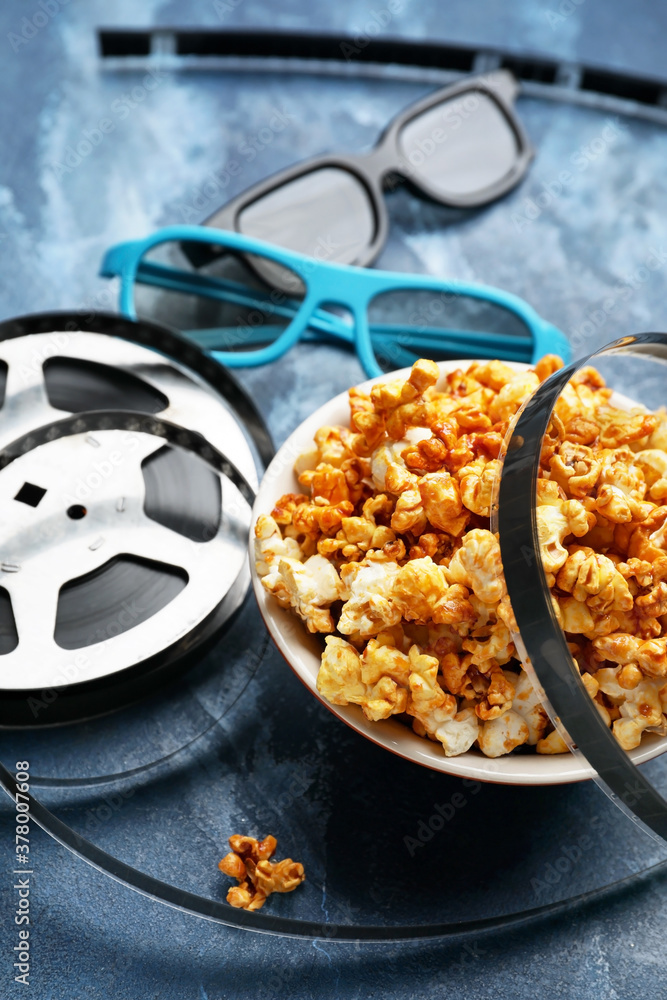 Popcorn with 3D glasses and film reel on color background