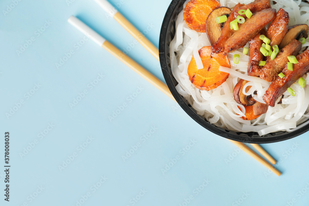 Bowl with tasty rice noodles and meat on color background