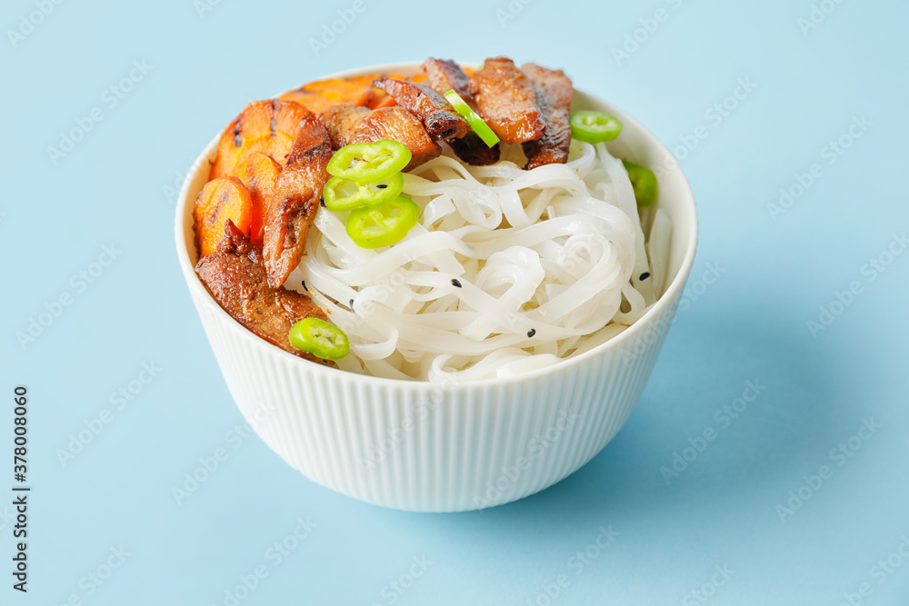 Bowl with tasty rice noodles and meat on color background