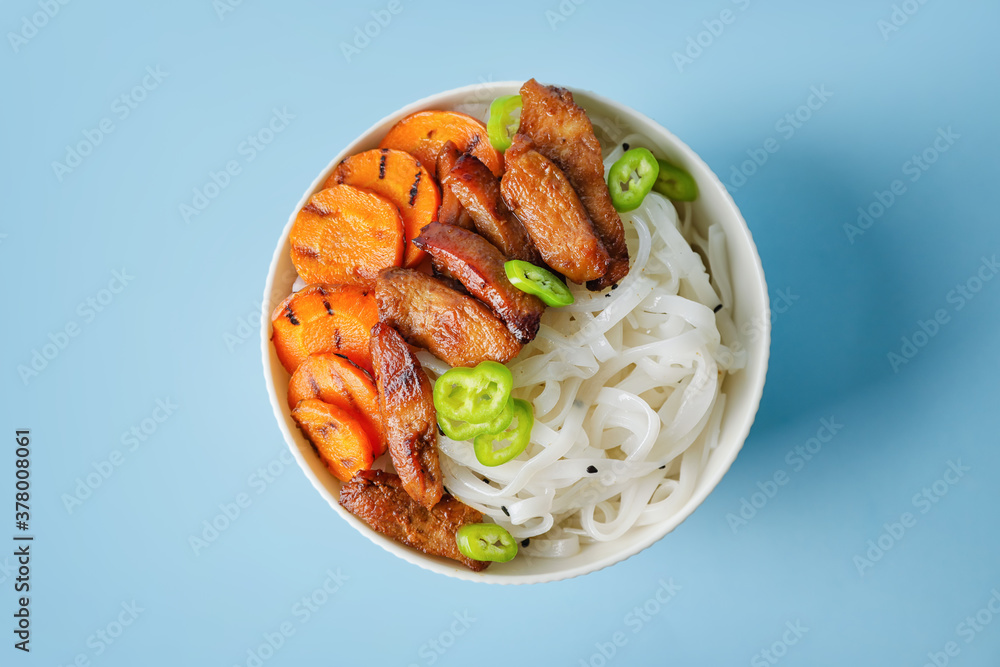 Bowl with tasty rice noodles and meat on color background