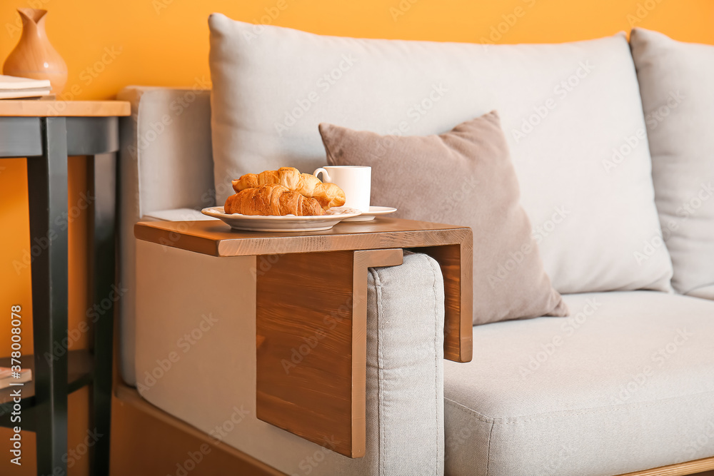 Cup of tea with croissants on armrest table in room