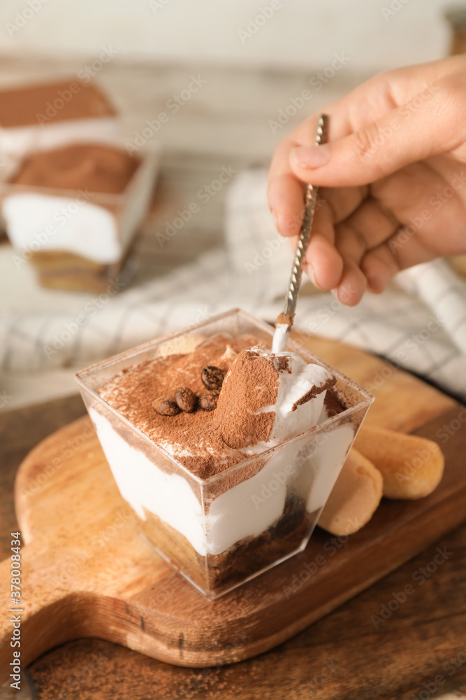 Woman eating sweet tasty tiramisu at table