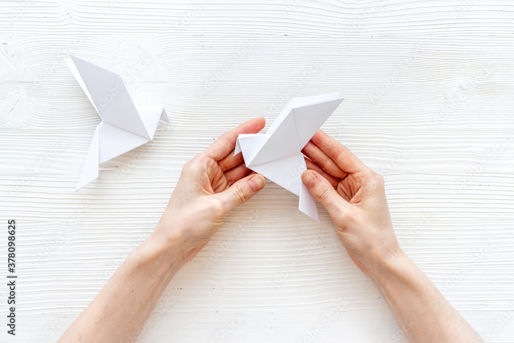 Female hands folding sheet of paper - origami bird. Overhead view