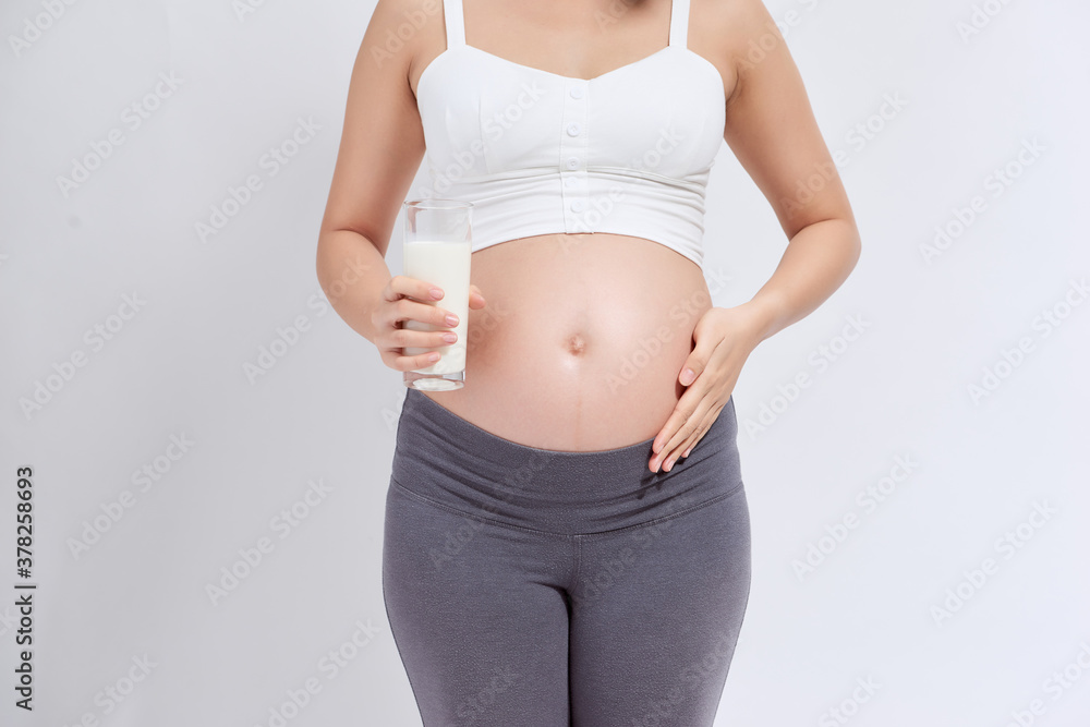 Happy pregnant woman drinking a glass of fresh milk and touching her belly