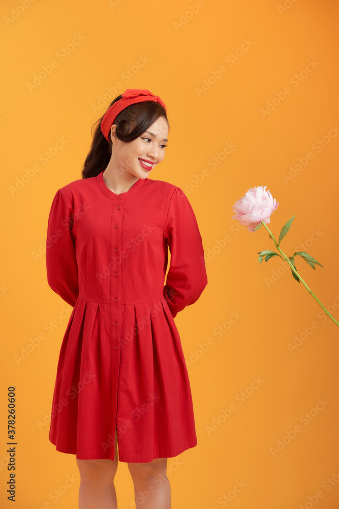 Charming young Asian in red dress holding peony flower isolated over orange background.