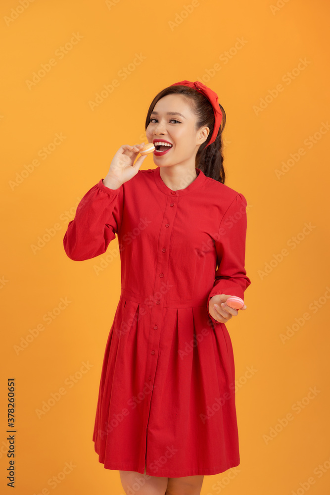 Young Asian woman over orange background holding colorful macarons isolated over orange background.