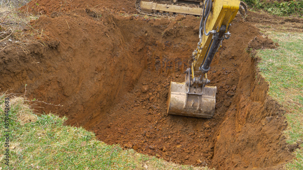 CLOSE UP: Yellow excavator digs out a deep hole in the middle of a meadow.