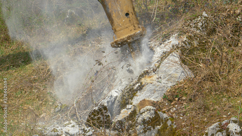 CLOSE UP: Big industrial jackhammer pounds a rock near a meadow in countryside.