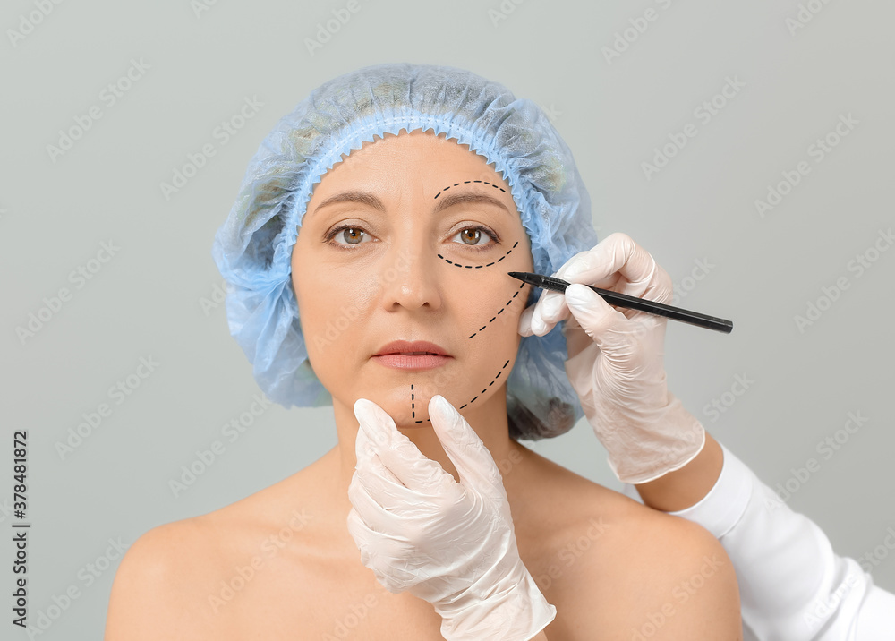 Plastic surgeon applying marks on womans face against grey background