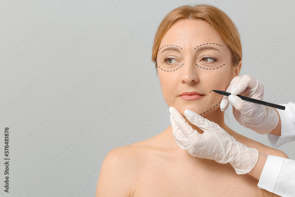 Plastic surgeon applying marks on womans face against grey background