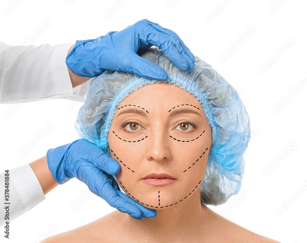 Plastic surgeon examining womans face against white background