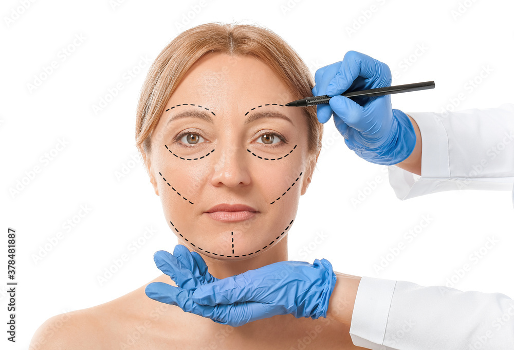 Plastic surgeon applying marks on womans face against white background