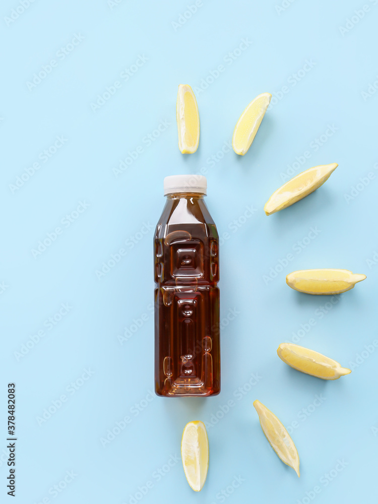 Bottle of fresh ice tea and lemon on color background