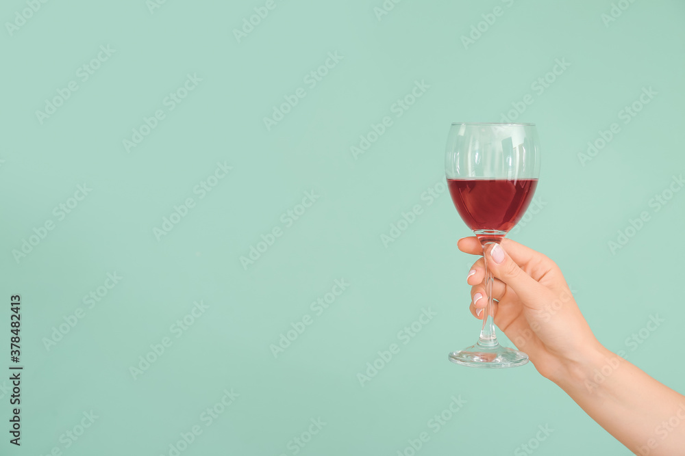 Hand with glass of wine on color background