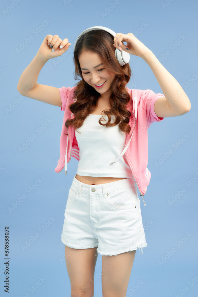 Amazing charming summer young woman in jeans shorts over colorful blue background. Dancing, listenin