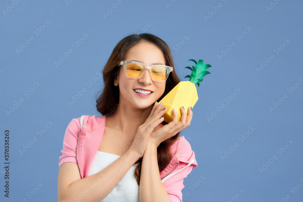 Young Asian woman holding paper pineapple over blue background.