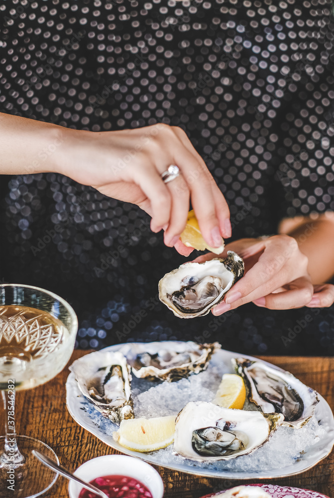 Hands of woman squeezing lemon juice to fresh Irish oysters over ice in plate and glass of champagne