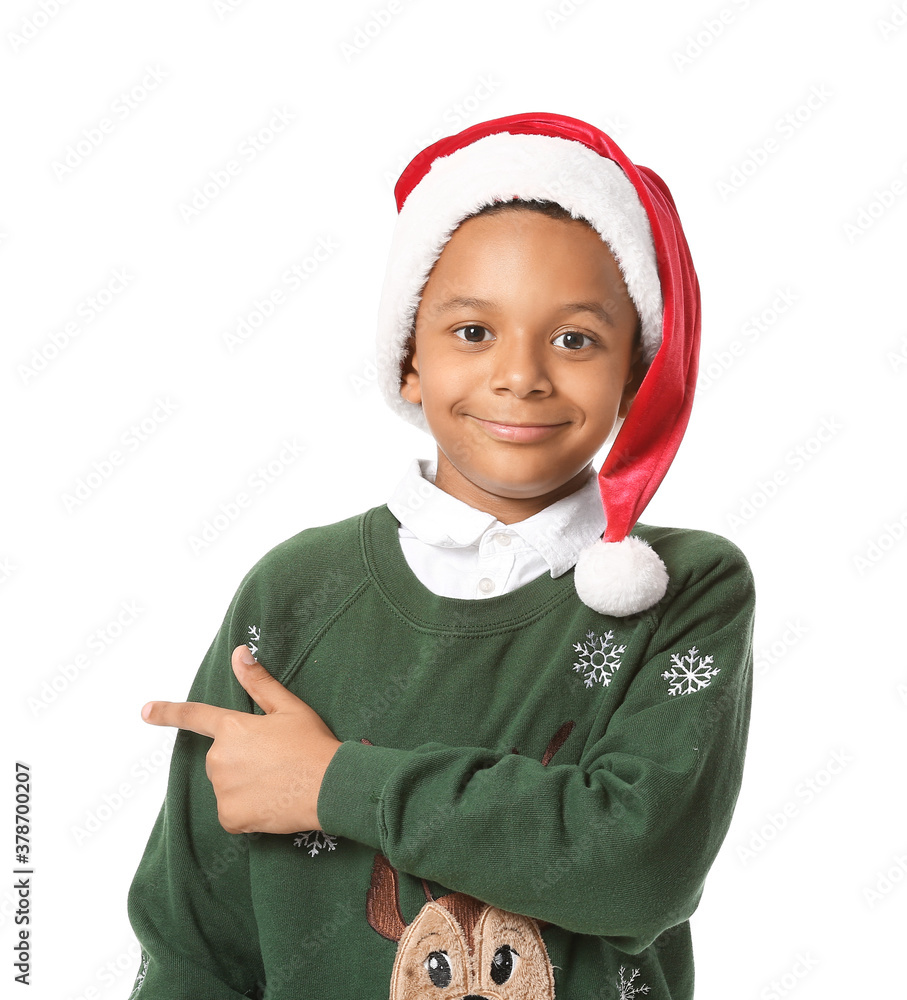 Cute African-American boy in Santa hat pointing at something on white background