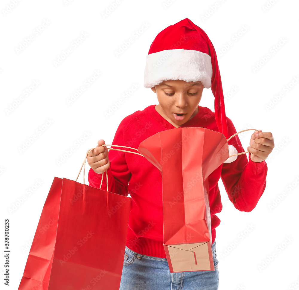 Cute African-American boy in Santa hat and with shopping bags on white background