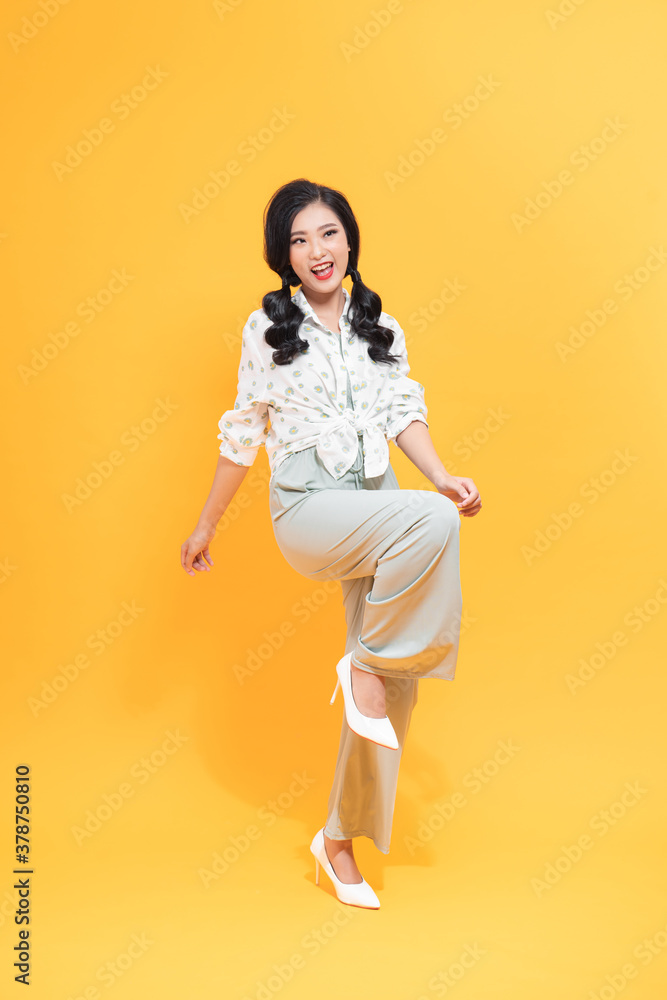 full length portrait of smiley stylish woman over yellow background