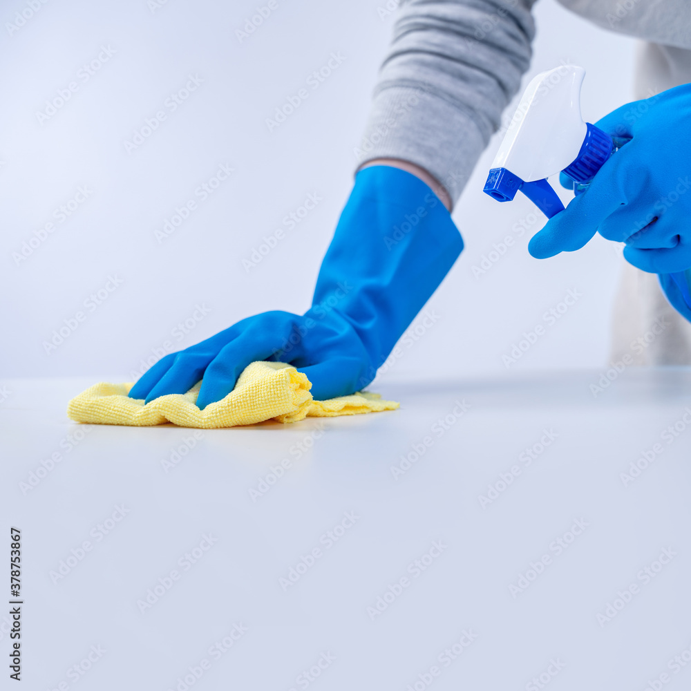 Young woman housekeeper in apron is cleaning, wiping down table surface with blue gloves, wet yellow