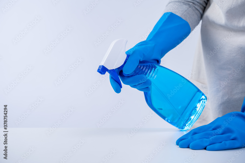 Young woman housekeeper in apron is cleaning, wiping down table surface with blue gloves, wet yellow