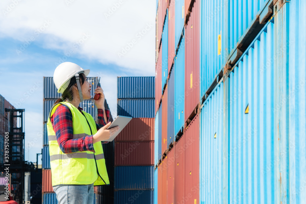 Engineer woman or Foreman manager in container depot working with digital tablet and walkie talkie f