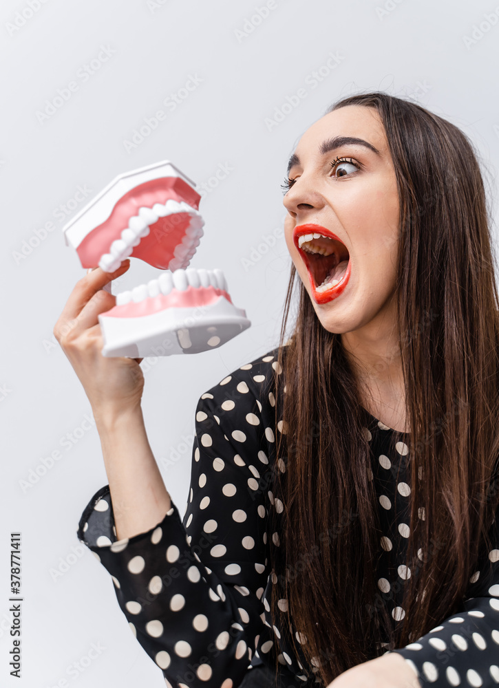 Funny girl toing with dental jaw on white background. Opened plastic jaw. Roaring girl with funny em