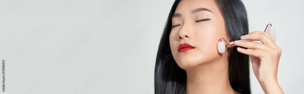 Face massage. Smiling woman using rose quartz facial roller for skin care, beauty treatment on white