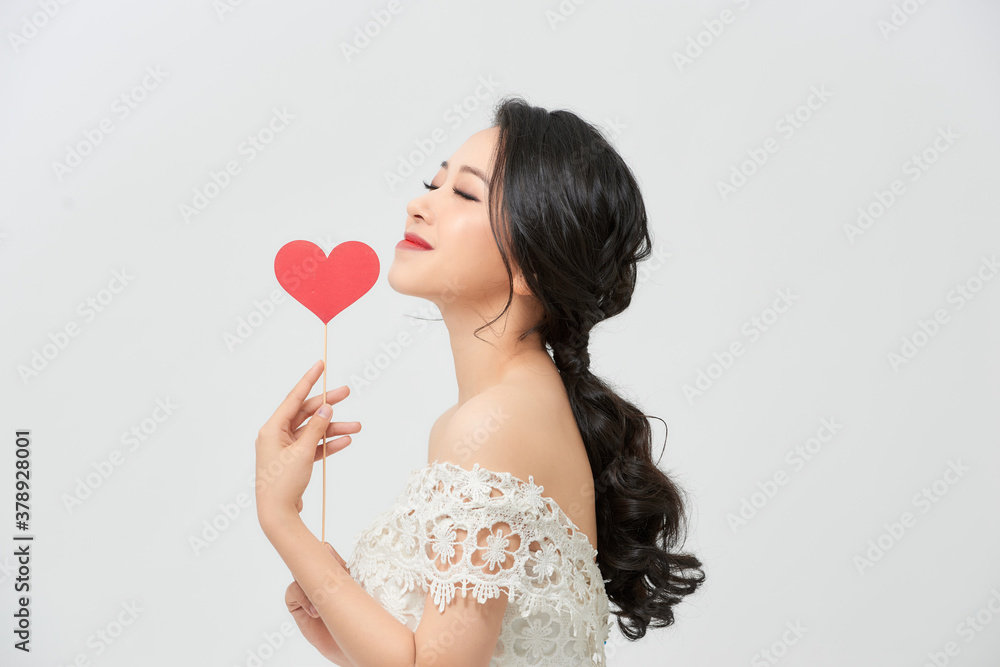 Asian woman in a wedding dress is holding  red heart on stick on a white background in the studio