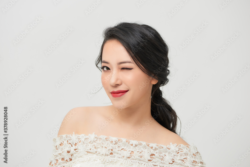 Portrait of cheerful young married woman winking to the camera while posing in white wedding dress.