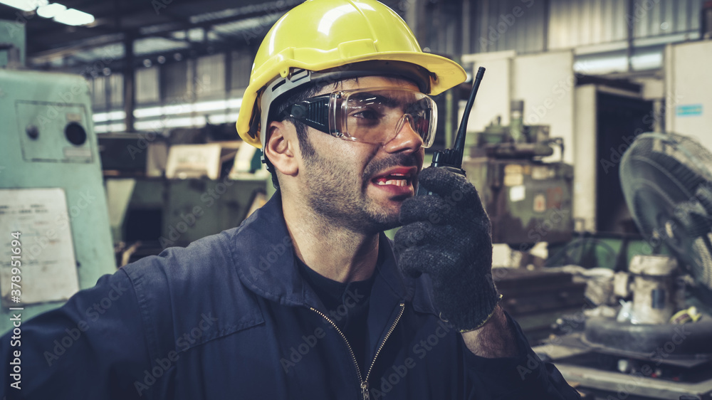 Factory worker talking on portable radio while inspecting machinery parts . Industrial and engineeri