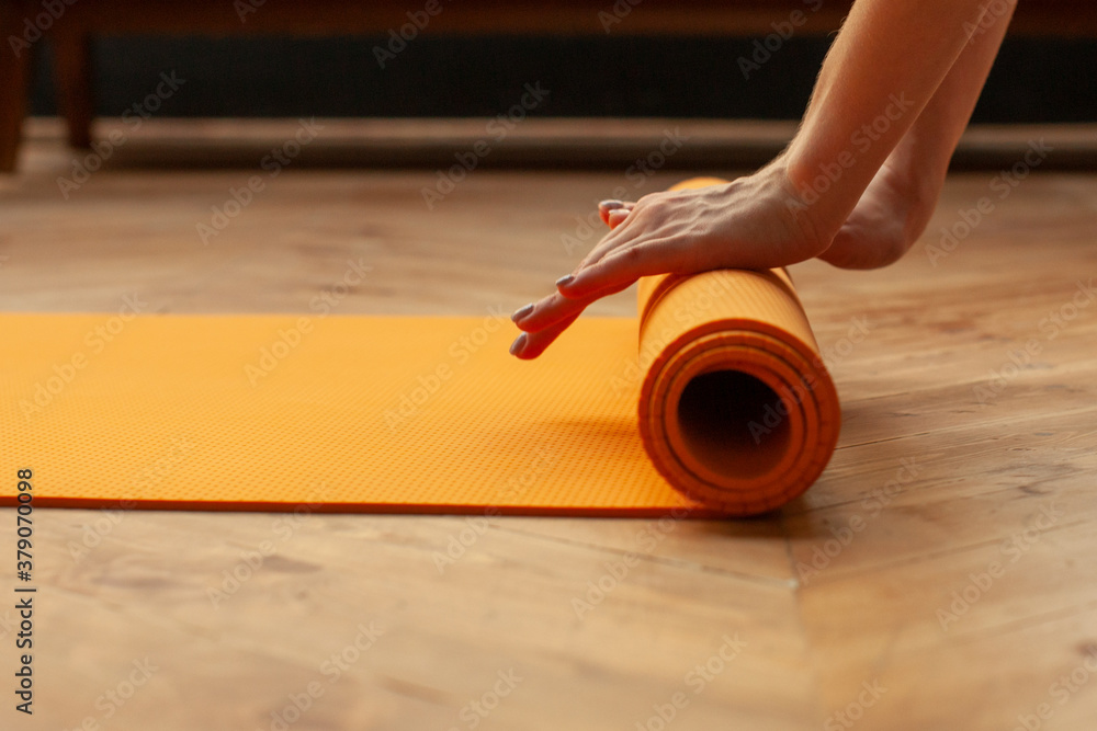 female hands unrolling yoga mat in home on parquet floor, preparing for yoga practice, detail shot