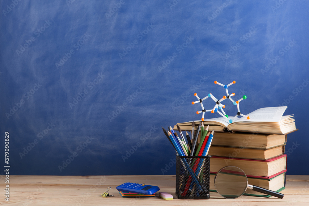 Education and sciences concept - books on the teacher desk in the auditorium, chalkboard on the back