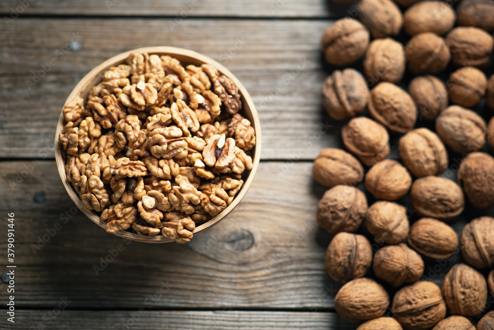 Fresh walnut kernels and whole walnuts in a bowl on rustic old wooden table. Healthy organic food, B