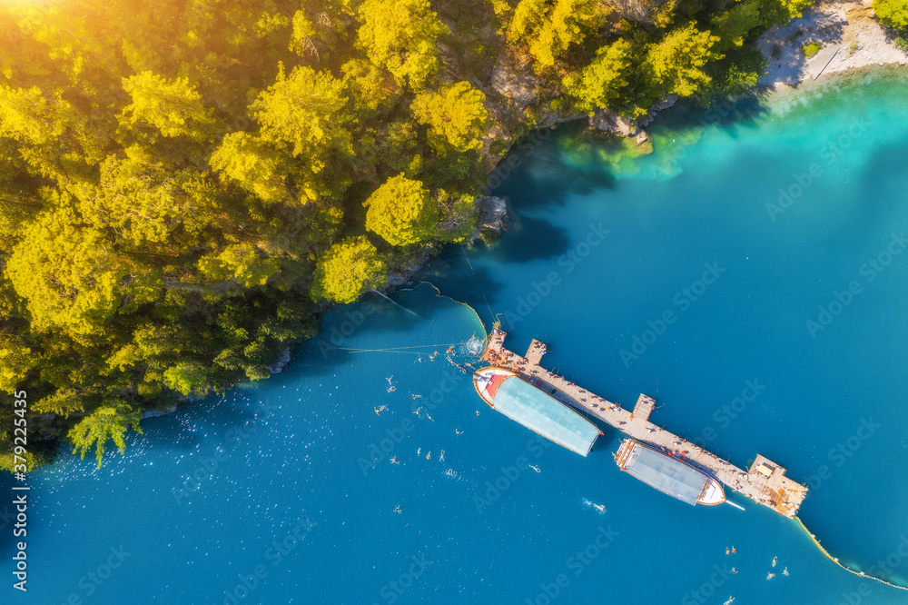 Aerial view of boats near wooden jetty in blue see and green trees at sunset in summer. Colorful lan